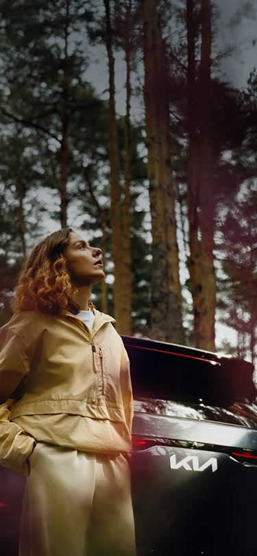 Eine Frau genießt die frische Frühlingsluft neben ihrem Kia EV5.