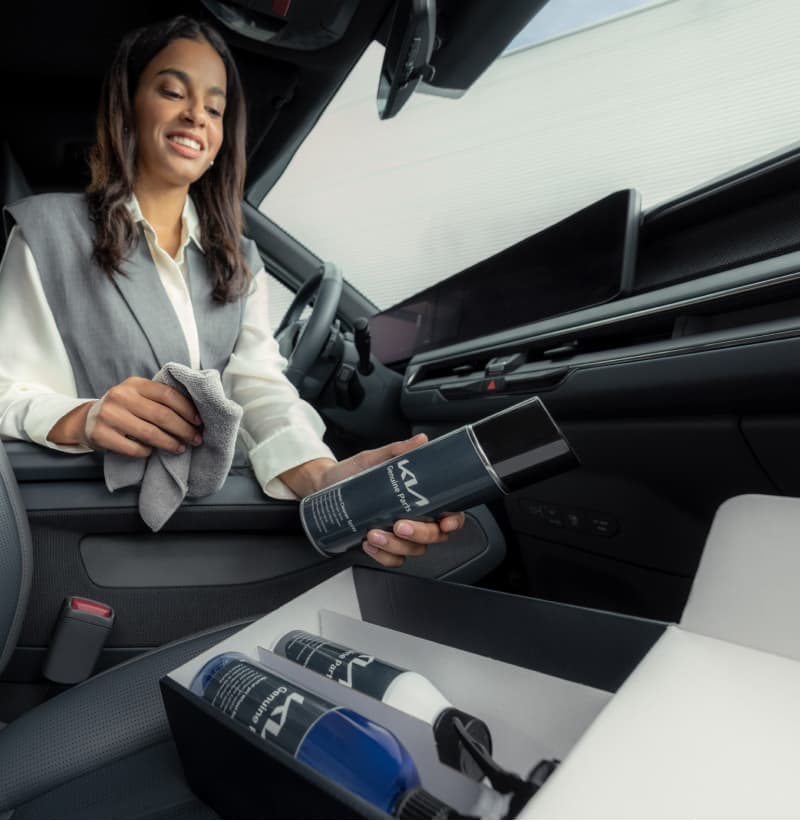 Eine Frau reinigt den Innenraum ihres Kia mit dem Kia Pflege Set.